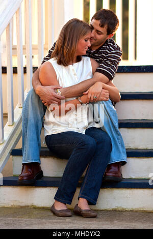 A young couple in love share a romantic embrace while sitting on steps of gazebo. Stock Photo