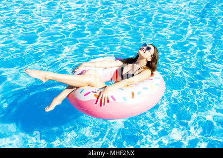 Beautiful young woman on inflatable donut in swimming pool. Stock Photo