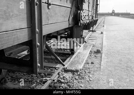 Main entrance to Auschwitz Birkenau Concentration Camp. In foreground, cattle car used to bring victims to the gas chambers. Monochrome photo. Stock Photo