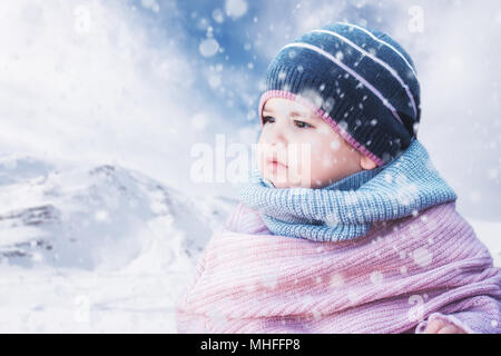 Cute baby girl wearing a warm winter hat and a colorful hat on a snowy background Stock Photo