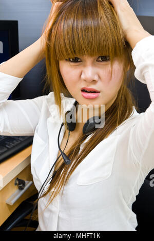Young tired business woman with headache sitting at computer in workplace holding head Stock Photo