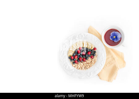 Healthy vegan breakfast bowl of oatmeal cereal with fruit (blueberries, bananas, cranberries) and nuts (almonds) with a cup of hibiscus herbal tea Stock Photo