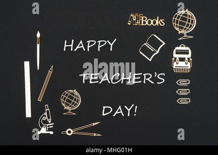 Concept back to school, text happy teacher's day with school supplies chipboard miniatures placed on blackboard Stock Photo
