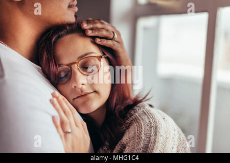 Close up of young couple in love embracing at home. Young woman leaning on man's chest with eyes closed. Stock Photo