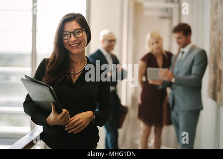 Portrait of smiling business woman with colleagues standing in background and discussing work. Asian female manager with coworkers at the back. Stock Photo
