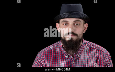 Pensive  bearded male dressed in a fleece shirt  and hat posing over black background. Stock Photo