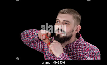Portrait of a funny man cutting his beards with scissors over black background. Stock Photo