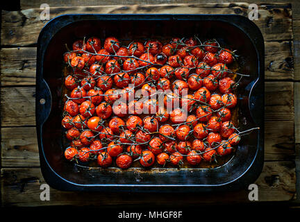 Ripe Cherry tomatoes branches roasted in a metallic oven dish over a rustic wooden table in a darkness ambient. Stock Photo