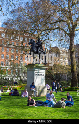 People sitting on the grass and eating lunch in a small city park, St James's Square Garden, London, UK Stock Photo