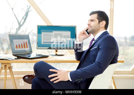 Portrait of young financial businessman analyzing financial data and consulting with his client on mobile phone. Stock Photo