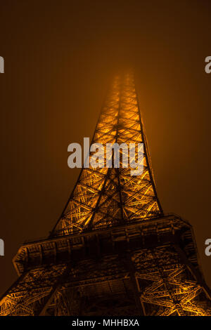 The Eiffel Tower at night with its summit in the fog / mist / clouds Stock Photo