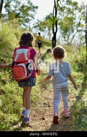 Mother and children walking through long grass through a forest in an inspiring scene, Mount Stuart hiking trails, Townsville, Queensland, Australia Stock Photo