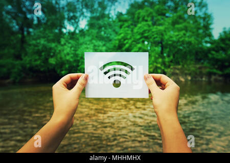 Woman hands holding a paper sheet with WiFi symbol in the middle of the nature with a river flowing near the forest. Dreaming of better WiFi, or excel Stock Photo