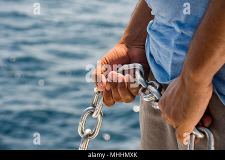 black indian man hands holding anchor chain on crystal water background Stock Photo