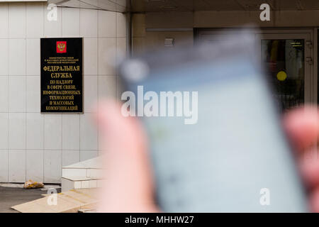 MOSCOW, RUSSIA - APRIL 30, 2018: Smartphone with Telegram app in hand on the background of a sign at the entrance to the Roskomnadzor building. After  Stock Photo