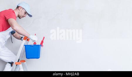 Painter Copy Space Photo Concept with Copy Space. Caucasian Painting Worker on the Small Metal ladder. Stock Photo