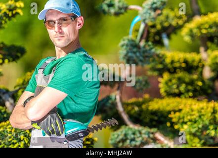 Professional Caucasian Gardener Portrait. Garden Worker with Compact Cordless Plants Trimmer. Stock Photo