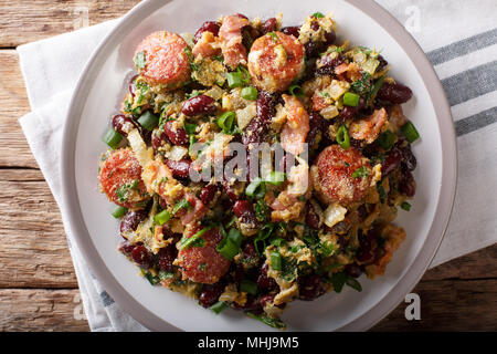 Brazilian beans with greens, sausages, bacon and eggs close-up on a plate on a table. Horizontal top view from above Stock Photo