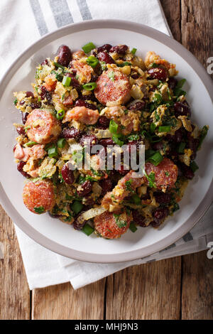 Brazilian beans with greens, sausages, bacon and eggs close-up on a plate on a table. Vertical top view from above Stock Photo