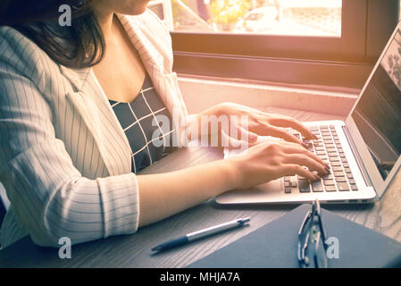 Business women type on notebook and have  memo book and pen and glass on the wood table Stock Photo
