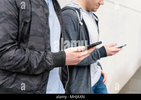 two antisocial mobile phone addicted male teenagers using smartphone, technology concept, leaning against wall with copy space Stock Photo