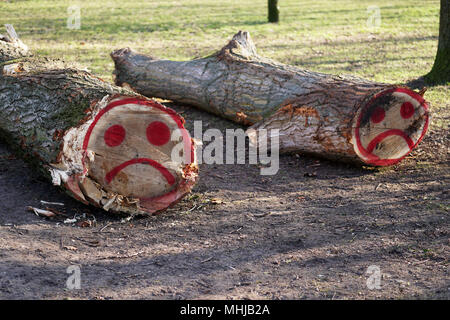 felled tree trunks with sad smiley face graffiti sprayed on them with red paint Stock Photo