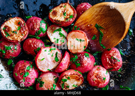 Beautiful roasted radishes in a pan with a wooden spoon close up Stock Photo