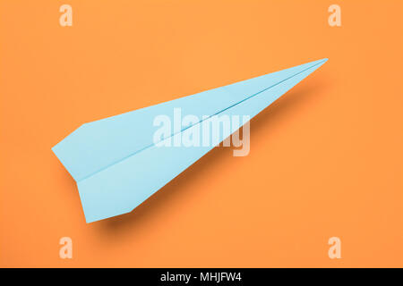 Blue paper plane on orange paper background. Top view Stock Photo