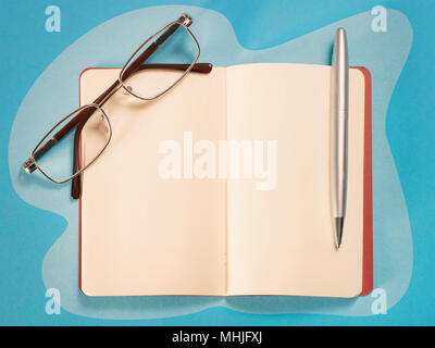 Open note, pen and eyeglasses top view on blue table. Soft toned sparse composition with copy space Stock Photo