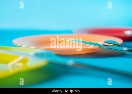 Festive colored plates and cutlery on blue table. Side view, selective focus Stock Photo