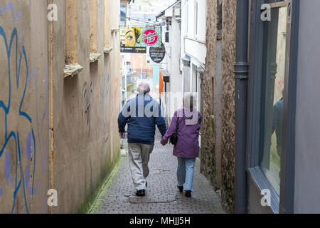 Elderly /senior couple walk hand in hand through narrow street in town Stock Photo