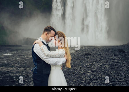 Iceland couple embrace near the big waterfall. Wall of the water on the background. Stock Photo