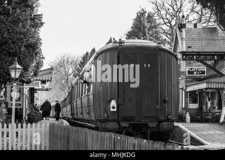 Black & white nostalgia. Rear view of vintage railway carriage pulled by steam engine waiting at SVR Hampton Loade station. Guard waves from window. Stock Photo