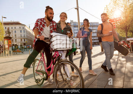 best friends having fun in the city hanging with bike skateboard and coffee to go. sunlight from right lens flares Stock Photo