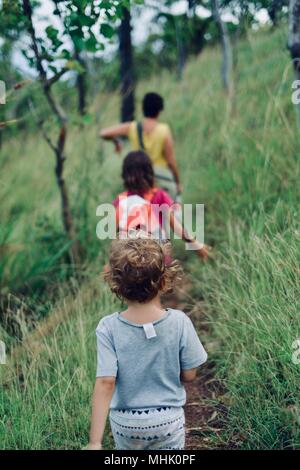 Mother and children walking through long grass through a forest in an inspiring scene, Mount Stuart hiking trails, Townsville, Queensland, Australia Stock Photo
