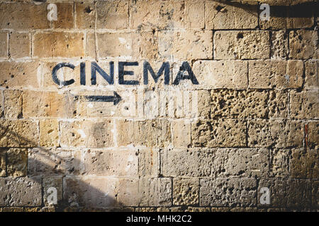 The word "cinema" and an arrow pointing the right side painted in black on a stone wall. Landscape format. Stock Photo