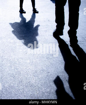Blurry silhouette shadows of a man and a woman walking toward each other on city street in the night Stock Photo