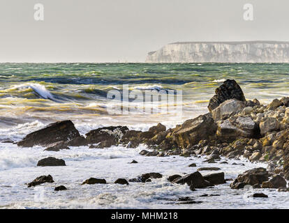 Rocky shoreline with rough seas and cliffs in the distance, Isle of Wight Stock Photo