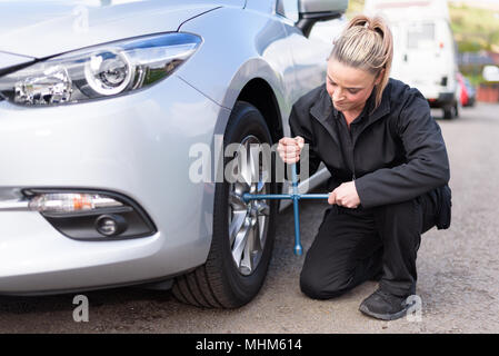 A woman mechanic loosening nuts on a wheel for a tire change Stock Photo