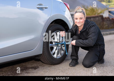 A woman mechanic loosening nuts on a wheel for a tire change, whilst looking at camera Stock Photo