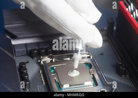 Hands wearing White Gloves with syringe applying thermal paste on the CPU processor on motherboard Close up Stock Photo