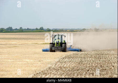 Tractor preparing land with plow, sunny summer day at agricultural field Stock Photo