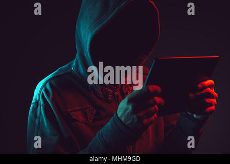Hooded computer hacker with tablet computer, red and blue light low key image Stock Photo