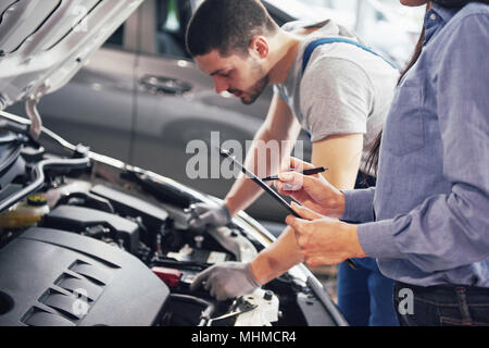 A man mechanic and woman customer look at the car hood and discuss repairs Stock Photo