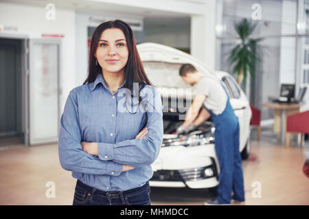 Woman at a car garage getting mechanical service. The mechanic works under the hood of the car Stock Photo