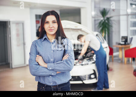 Woman at a car garage getting mechanical service. The mechanic works under the hood of the car Stock Photo