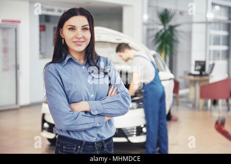 Woman at a car garage getting mechanical service. The mechanic works under the hood of the car Stock Photo