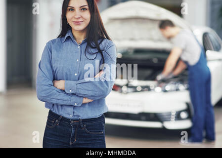 Woman at a car garage getting mechanical service. The mechanic works under the hood of the car Stock Photo