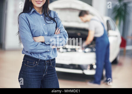 Woman at a car garage getting mechanical service. The mechanic works under the hood of the car Stock Photo