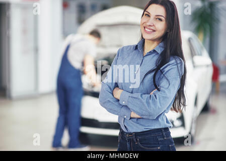 Woman at a car garage getting mechanical service. The mechanic works under the hood of the car Stock Photo